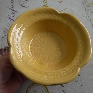 May include: A yellow ceramic bowl with a decorative floral design. The bowl has a scalloped edge and a smooth, glossy finish.