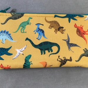 May include: A yellow zippered pouch with a dinosaur print. The pouch is filled with various dinosaurs, including a stegosaurus, a brachiosaurus, a triceratops, and a pterodactyl.