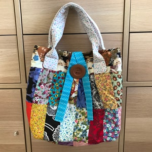 May include: A patchwork tote bag with a blue ribbon and a brown button. The bag is made of different fabrics with floral patterns.