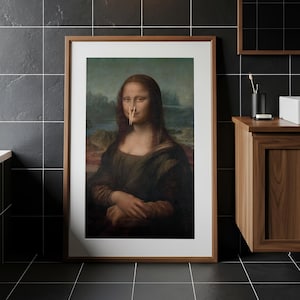 Può includere: Una stampa incorniciata della Gioconda con una molletta di legno attaccata al naso, esposta in un bagno con pareti piastrellate nere, una vasca bianca, un mobile in legno e una lampada da parete sopra l'opera d'arte.