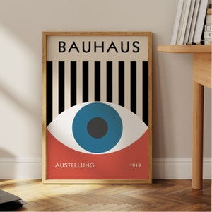 May include: A framed Bauhaus art print featuring a stylized eye design. The artwork includes the word "BAUHAUS" in black, vertical black and white stripes, a blue eye, and the words "AUSSTELLUNG 1919" in red.