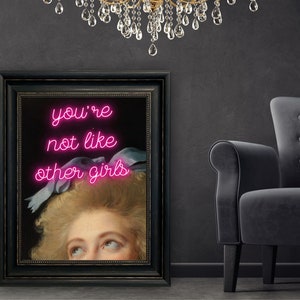 May include: A framed print of a painting of a woman with a pink neon sign that reads "you're not like other girls".