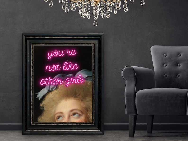May include: A framed print of a painting of a woman with a pink neon sign that reads "you're not like other girls".