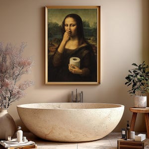 May include: A framed print of the Mona Lisa holding a roll of toilet paper, with her finger on her nose. The artwork is in a gold frame and hangs above a large, stone-like bathtub.