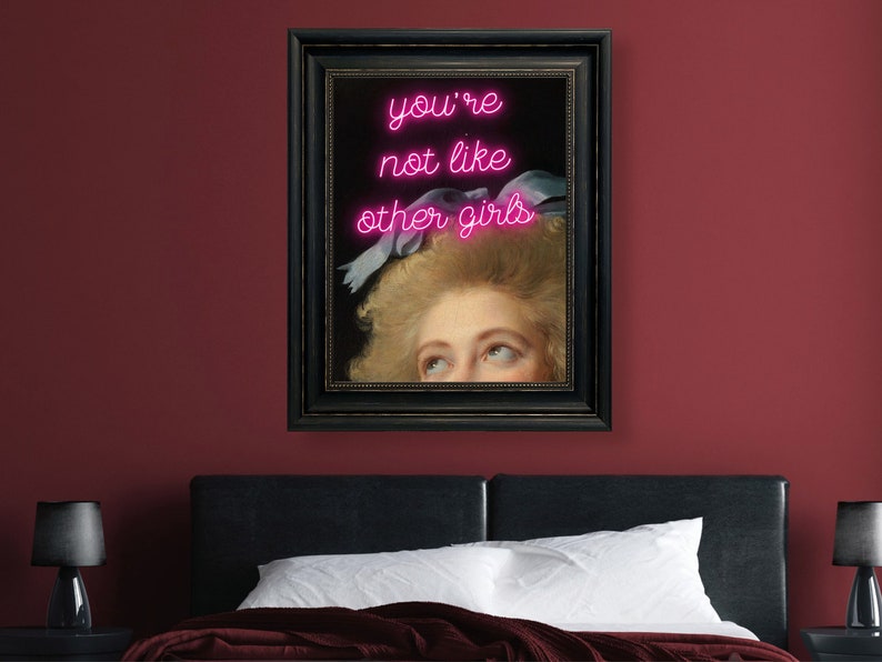 May include: A framed print of a woman's face with pink neon text that reads "you're not like other girls" above her head.
