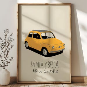 May include: Framed art print depicting a yellow vintage car with a black roof. The Italian phrase "La Vita è Bella" and the English translation "life is beautiful" are written below. The artwork has a minimalist style, with a cream background.