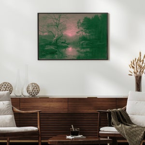 May include: A framed landscape art print featuring a serene forest scene with a river. The artwork has a color palette of green and pink, with a large tree in the foreground and a deer near the water. The print is displayed above a wooden cabinet.