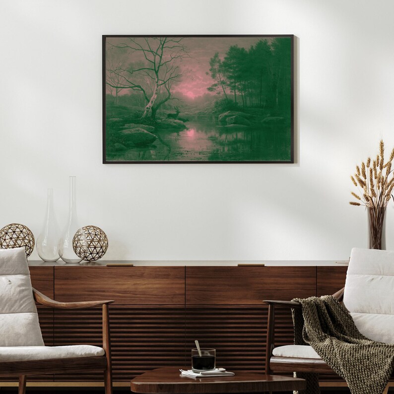 May include: A framed landscape art print featuring a serene forest scene with a river. The artwork has a color palette of green and pink, with a large tree in the foreground and a deer near the water. The print is displayed above a wooden cabinet.