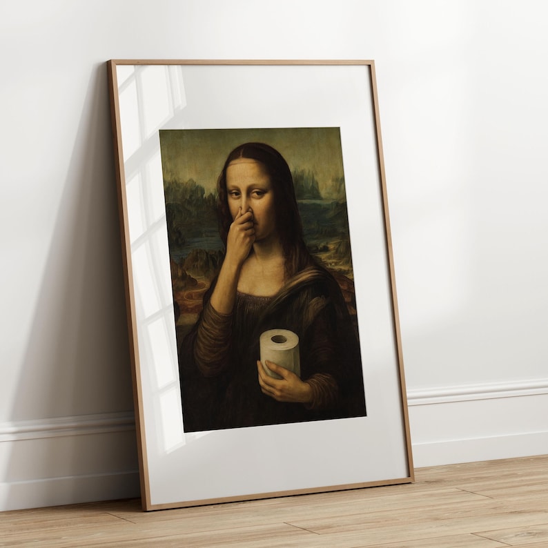 May include: Framed print of the Mona Lisa, altered to depict her pinching her nose and holding a roll of toilet paper. The artwork is in a wooden frame, leaning against a white wall and wooden floor.