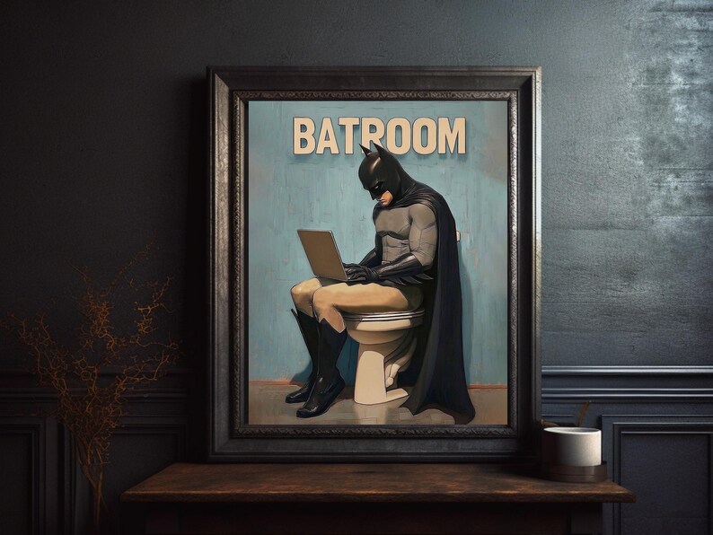 May include: A framed illustration of a superhero in a black cape and mask sitting on a toilet with a laptop on their lap. The text "BATROOM" is printed above the superhero.