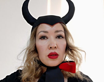 May include: A woman wearing a black devil costume with red accents. The costume includes a black hat with horns and a black and red bow tie.