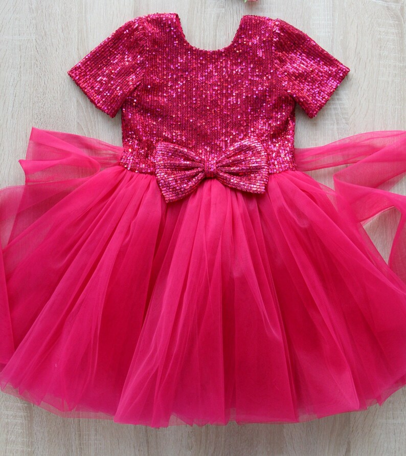 May include: A pink tulle dress with a sequined bodice and a large pink bow at the waist.