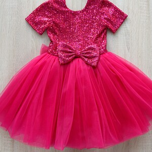 May include: A pink tulle dress with a sequined bodice and a large bow at the waist.