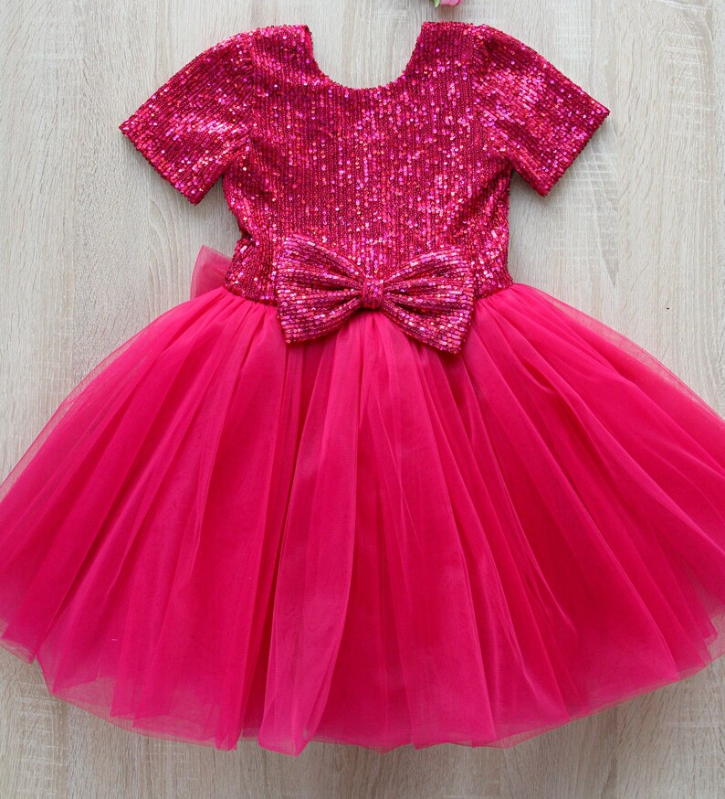 May include: A pink tulle dress with a sequined bodice and a large bow at the waist.