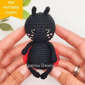 May include: A black crocheted ladybug with red wings and pink cheeks. The ladybug is sitting on a white surface.