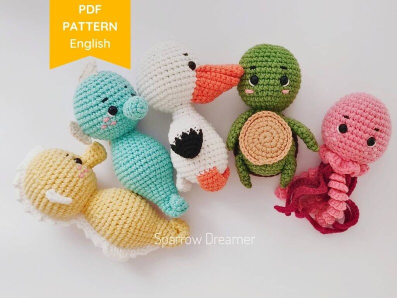 Op de afbeelding: Een verzameling handgemaakte gehaakte zeedieren, waaronder een zeepaardje, een eend, een schildpad en een kwal. De speelgoedjes zijn in verschillende kleuren, zoals blauw, geel, groen, wit en roze. De afbeelding bevat de tekst "PDF PATTERN English" en de naam "Sparrow Dreamer".