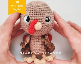 May include: A crocheted turkey amigurumi toy with brown and red yarn. The toy has a red wattle, brown feathers, and black eyes. The toy is being held by two hands.