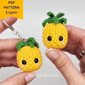 May include: Two yellow crochet pineapple keyrings with green tops and black eyes. One keyring is attached to a silver ring. The text "PDF PATTERN English" is in a yellow banner. The text "Sparrow Dreamer" is at the bottom.