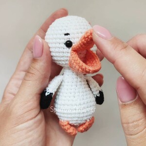 Op de afbeelding: Een handgemaakte witte gehaakte eend met een oranje snavel en poten, en zwarte accenten op de vleugels. De eend heeft een rond lichaam en hoofd, en kleine zwarte ogen. De tekst "Sparrow Dreamer" is zichtbaar.