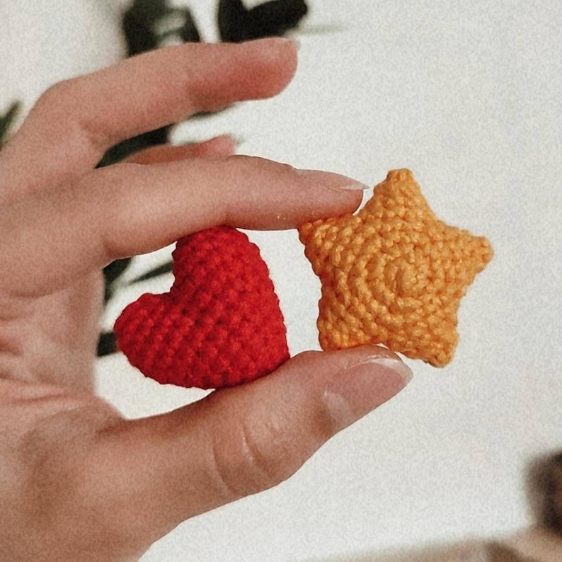 Puede incluir: Un coraz&oacute;n rojo y una estrella amarilla de ganchillo se muestran. El coraz&oacute;n es de un rojo s&oacute;lido, la estrella de un amarillo-naranja brillante. Ambos est&aacute;n hechos con un punto de ganchillo texturizado, lo que sugiere artesan&iacute;a hecha a mano.