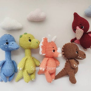 May include: A set of six crocheted stuffed animals, including a blue dinosaur, a green dinosaur, an orange triceratops, a brown dinosaur, a red pterodactyl, and a white cloud.