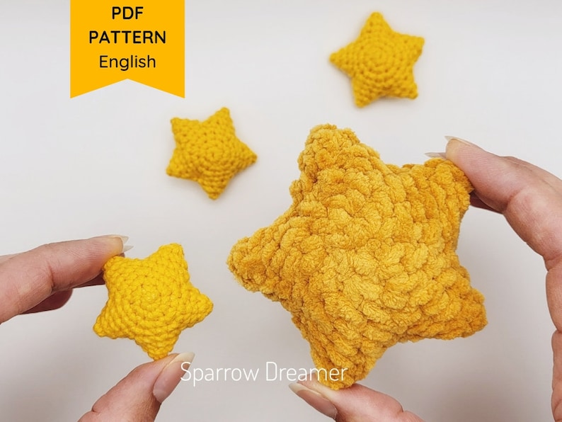 Puede incluir: Cuatro estrellas amarillas de ganchillo de diferentes tama&ntilde;os se muestran sobre un fondo blanco. Las estrellas est&aacute;n hechas a mano con una puntada texturizada, y el texto "PDF PATTERN English" est&aacute; en la esquina superior izquierda. El logotipo de Sparrow Dreamer est&aacute; en la esquina inferior derecha.