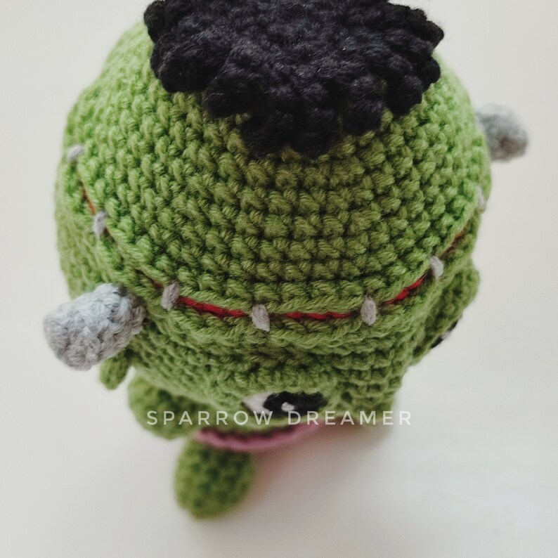 May include: Green crocheted Frankenstein monster toy with black hair, red stitching, and gray ears. The toy has black eyes and a pink mouth. The text "SPARROW DREAMER" is visible on the toy.