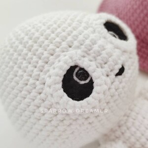May include: White crocheted amigurumi ghost with black eyes. The ghost is holding a pink crocheted heart.