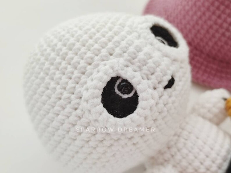 May include: White crocheted amigurumi ghost with black eyes. The ghost is holding a pink crocheted heart.