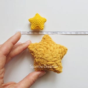 Puede incluir: Dos adornos amarillos en forma de estrella de ganchillo. La estrella m&aacute;s grande mide aproximadamente 13 cm de di&aacute;metro, y la estrella m&aacute;s peque&ntilde;a mide unos 5 cm. Las estrellas est&aacute;n hechas de un hilo suave y texturizado. La imagen est&aacute; tomada sobre una superficie blanca.