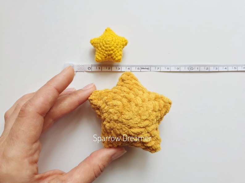 Puede incluir: Dos adornos amarillos en forma de estrella de ganchillo. La estrella m&aacute;s grande mide aproximadamente 13 cm de di&aacute;metro, y la estrella m&aacute;s peque&ntilde;a mide unos 5 cm. Las estrellas est&aacute;n hechas de un hilo suave y texturizado. La imagen est&aacute; tomada sobre una superficie blanca.