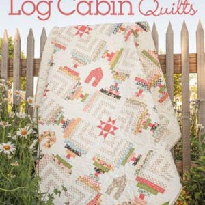 May include: A book titled "Creative Log Cabin Quilts" with a white quilt featuring a log cabin pattern in red, green, blue, and yellow on the cover. The quilt is draped over a white picket fence with a flower garden in the foreground. The book cover also features the text "Annie's Quilting" and "10 Fresh New Designs".