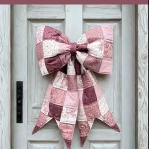 May include: A large quilted bow made of fabric squares in various shades of pink, mauve, and white with floral and geometric patterns. The text on the image reads: THE BIG GIANT QUILTED BOW, Designed to be reversible, Scrappy and fat quarter friendly, 3 style options included, A beginner-friendly sewing pattern + video tutorial by: LGC LINDSEY GRACE CREATES.