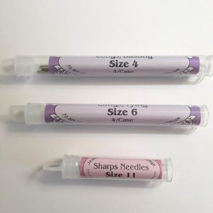May include: Three clear plastic tubes of sewing needles. The top tube reads "Size 4" and the middle tube reads "Size 6". The bottom tube is labeled "Sharps Needles Size 11". Each tube has a purple and white label.