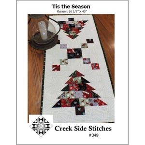 May include: A quilted Christmas runner with a cream background and two Christmas tree designs. The runner is 16.5 inches by 40 inches and features the text "Tis the Season". The trees are made of red, green, and black patterned fabric.