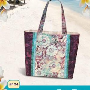 May include: A colorful tote bag with a floral pattern and turquoise accents. The bag has six pockets inside and is fat quarter friendly. The bag is labeled "Fiji Tote" and is designed by Nancy Green for Pink Sand Beach Designs.