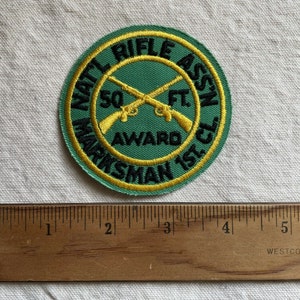May include: A green and yellow embroidered patch with the text "NAT'L RIFLE ASS'N 50 FT AWARD MARKSMAN 1ST. CL."