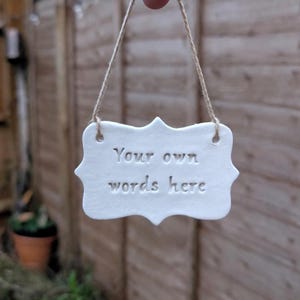 May include: A white ceramic sign with the text "Your own words here" in a decorative font. The sign is suspended by a natural twine string. The background is a wooden fence.