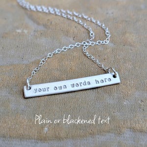 May include: A silver-colored horizontal bar necklace featuring a delicate chain and a rectangular pendant. The pendant is stamped with the text 'your own words here' in lowercase letters. The text 'Plain or blackened text' appears below the pendant.