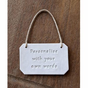 May include: White rectangular sign with rounded corners and the text "Personalise with your own words" embossed on the front. A natural twine loop is attached for hanging. The sign is on a wooden surface.
