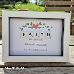 May include: A white framed picture with a heart and the word "FAITH" spelled out with Scrabble tiles. The quote "Sees the invisible, believes the unbelievable, and receives the impossible" is written below the tiles.