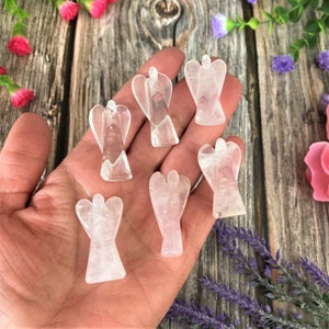 May include: Six clear quartz angel figurines, carved from crystal, are displayed on a hand. The angels are approximately 5 cm tall and have a delicate, ethereal appearance.