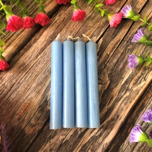 May include: Four light blue pillar candles on a wooden surface. The candles are arranged in a row and are all the same size.