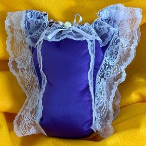 May include: Purple satin pillow with white lace trim and a small white flower accent.