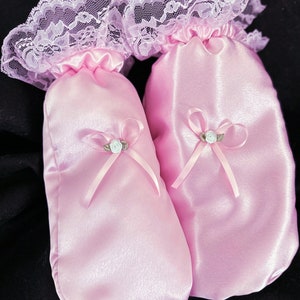 May include: A pair of pink satin hand warmers with lace trim and a satin bow with a small flower accent.