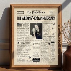 May include: A framed print of a newspaper front page celebrating "The Wilsons' 40th Anniversary." The print features a black and white photo of a couple, along with text detailing events and costs from 1986. The frame is made of light brown wood.