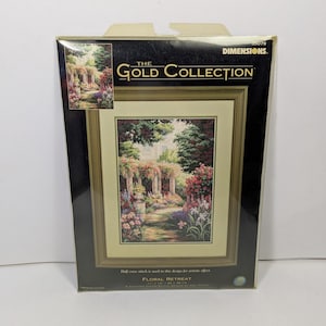 May include: A Dimensions The Gold Collection cross stitch kit titled Floral Retreat. The packaging features a finished garden scene with stone pillars, pink and purple flowers, and green trees. It measures 11 inches by 16 inches.