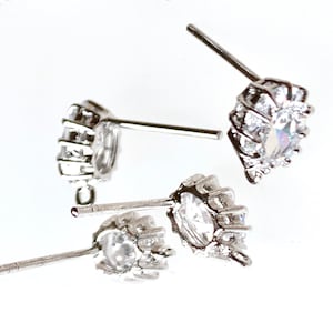 May include: Four pairs of silver stud earrings with clear cubic zirconia stones. The earrings are arranged in a random pattern on a white surface.