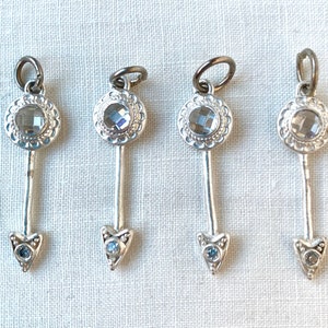 Può includere: Quattro ciondoli a forma di freccia argentati con accenti di cristallo trasparente e accenti di pietre preziose blu. I ciondoli sono circa delle dimensioni di una moneta da un centesimo di euro.