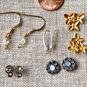 May include: Assortment of earring findings and components, including gold-tone and silver-tone earring hooks, gold-tone flower-shaped charms, and black metal round charms with clear rhinestones.  There are also two small gold-tone round charms with clear rhinestones.